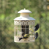 Hanging outdoors the feeder has birds enjoying the seeds from inside.