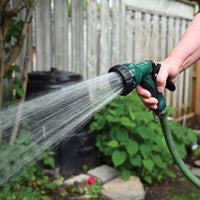 Green nozzle is attached to hose while watering plants outdoors.
