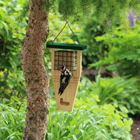 Feeder is hanging on a tree outside while a woodpecker is eating a suet cake from the cage of the feeder.