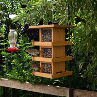 The feeder is outdoors hanging while two birds eat from the seeds it provides.