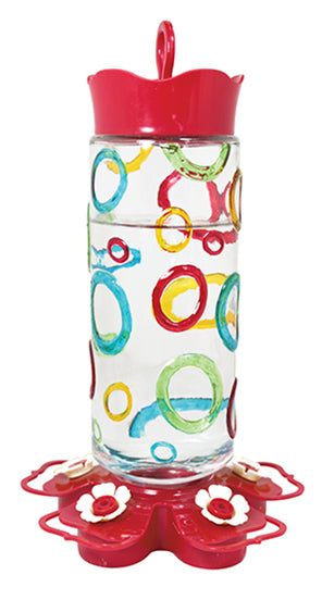 Red circular lid and base. Base has white flower shaped feeding holes. Glass has blue, red, yellow, and green coloured rings on it.