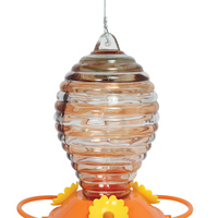 Clear glass for the nectar is painted with orange stripes, the glass is a oval shape, there is an orange circular base with yellow flower shaped feeding holes.
