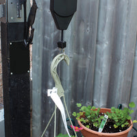 Hanging device is attached to a pole outdoors where it is holding up a plant that is hooked on the bottom ring.