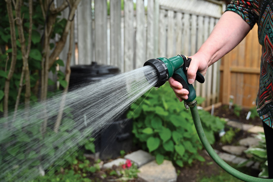 Green nozzle is attached to hose while watering plants outdoors. 
