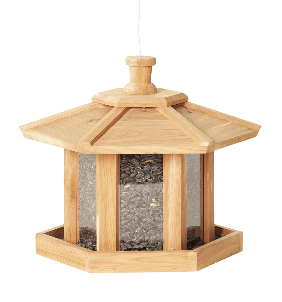 Beige wooden gazebo shaped bird feeder that is filled with seeds.