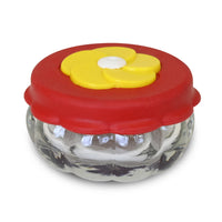 Small circular jar, red lid with a yellow flower shaped feeding hole. 