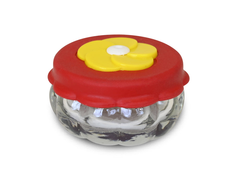 Small circular jar, red lid with a yellow flower shaped feeding hole. 