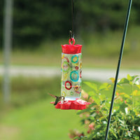 Outdoors hanging while a hummingbird is enjoying nectar from the feeder.