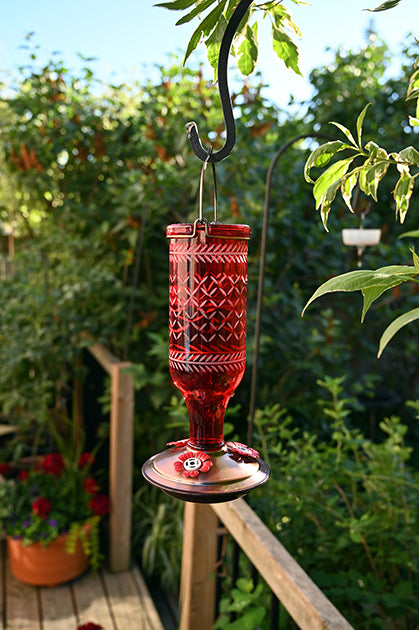 Red upside down bottle shape, has white line designs on it. Copper coloured circular base with red flower shaped feeding holes. 
